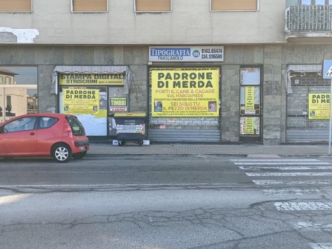 Troppi escrementi sui marciapiedi e un tipografo di Serravalle Scrivia incolla sulla vetrina un manifesto: “Padroni di m…”